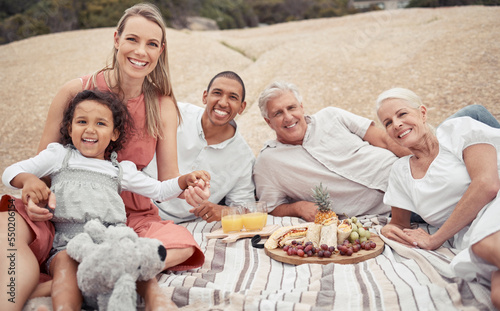 Portrait  love and happy interracial family having a picnic on the beach and smile while having some food with snacks. Bonding on a day out at the beach on tropical vacation holiday in summer