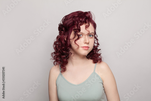 Beautiful woman with red curly hair in grey top on white studio wall background