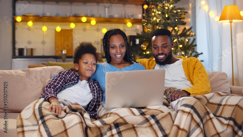 African-American couple and son sitting on couch having videocall with family on christmas eve