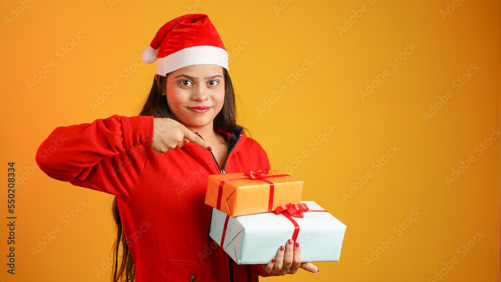 Beautiful young woman with Christmas gift box, Asian Indian girl wearing Santa cap isolated over colour studio background Beautiful young woman with Christmas gift box, Asian Indian girl wearing Santa cap isolated over colour studio background