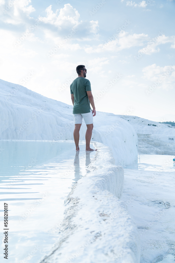 Unrecognizable tourist with beard and sunglasses gazing at the horizon with his feet sunk in the thermal pools of pamukkale.