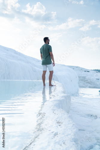 Unrecognizable tourist with beard and sunglasses gazing at the horizon with his feet sunk in the thermal pools of pamukkale.
