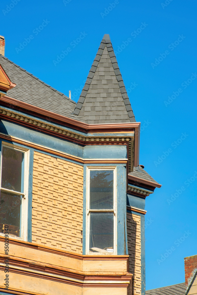 Victorian style house with spire type rooftop and brown wooden slatted timber house in a downtown or suburban neighborhood