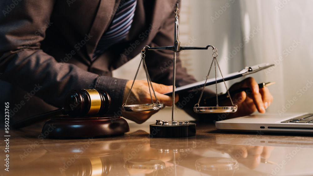 Justice and law concept.Male judge in a courtroom with the gavel, working with, computer and docking keyboard, eyeglasses, on table in morning light Justice and law concept.Male judge in a courtroom with the gavel, working with, computer and docking keyboard, eyeglasses, on table in morning light
