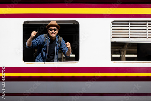 Young asian man travel by train. Sticking his head outta the train window. Explorer Backpacker arrival and departure at platform railway. Freedom  trip on vacation time holiday weekend. photo