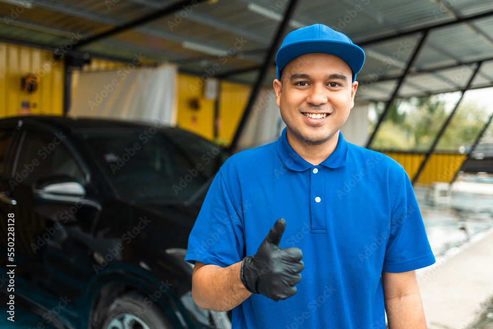 Man worker in uniform washing standing front car service station. Car