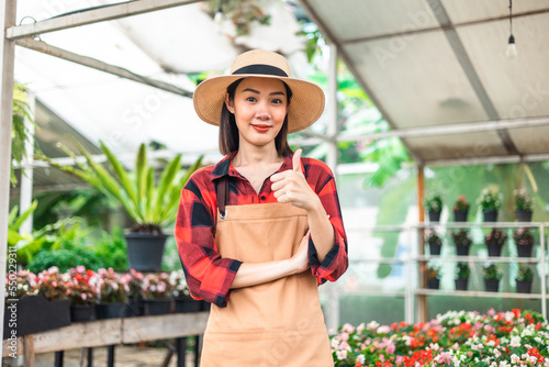 Happy gardener woman in gloves plants flowers in greenhouse using tablet check growth quality of Plant. Florists woman working gardening in the backyard. Flower care harvesting. © Chanakon