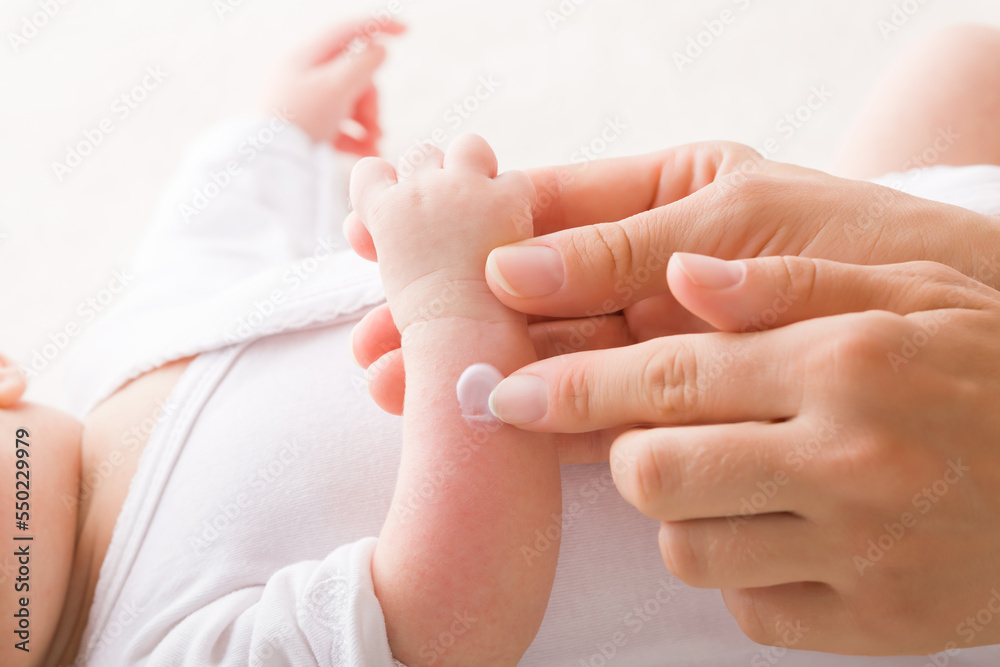 Young adult mother finger applying white medical ointment on newborn arm. Red rash on skin. Allergy from milk formula or mother milk. Care about baby body. Closeup. Side view. - obrazy, fototapety, plakaty 
