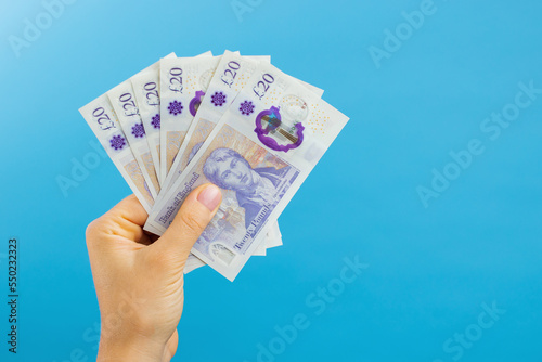 Image woman's hands which holds British pounds in her hands isolated over blue studio background.