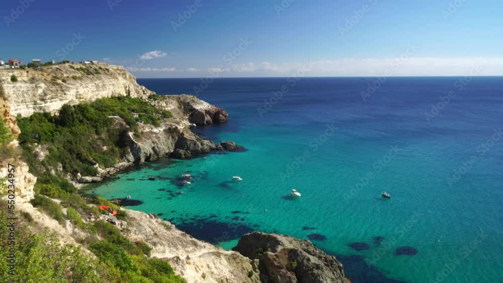 Boats and yachts in the rocky bay with crystal clear azure sea on a sunny day. The concept of an ideal place for summer travel and relaxation. Boats and yachts in the rocky bay with crystal clear azure sea on a sunny day. The concept of an ideal place for summer travel and relaxation.