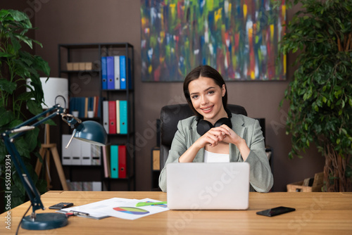 Vászonkép Photo of delighted young woman wearing headphones looking at camera smiling sitting at desk in front of computer laptop working studing process from home