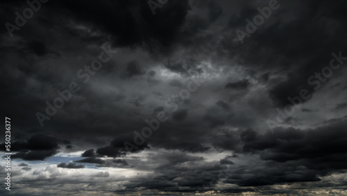 dark dramatic sky with black stormy clouds before rain or snow as abstract background, extreme weather, the sun shines through the clouds, high contrast photo