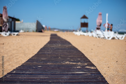 Wooden beach path made of dark boards on light sand on the sea beach, selected focus.