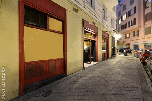 Facade of a local bar with a yellow facade and metal windows painted in red