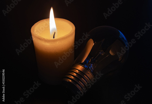Burning candle near not glowing light bulb in darkn home. Blackout city, power cut, load shedding, energy crisis or power outage, symbolic image. photo