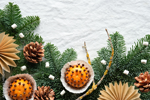 Fragrant pomander balls handmade from tangerines with cloves. Handmade paper stars from brown paper. Flat lay on off white textile with fir twigs. Copy-space on paper card with envelope in hand.