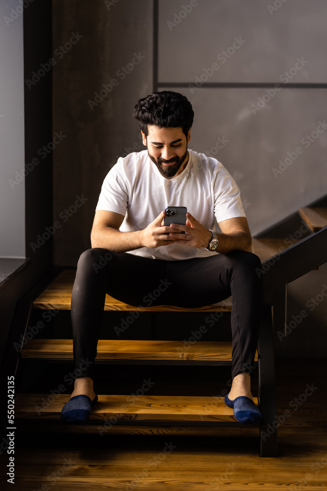 Business man sitting indoors on stairs near flower pots with plants and use phone.