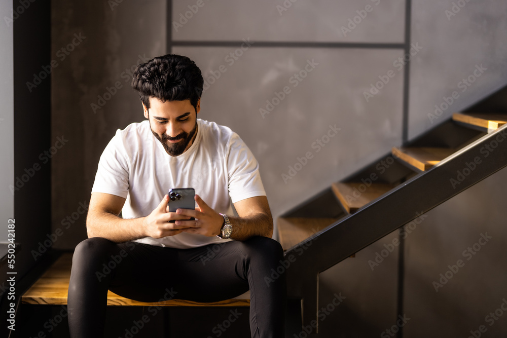 Business man sitting indoors on stairs near flower pots with plants and use phone.