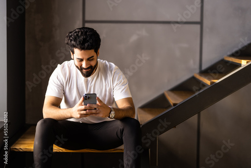 Business man sitting indoors on stairs near flower pots with plants and use phone.