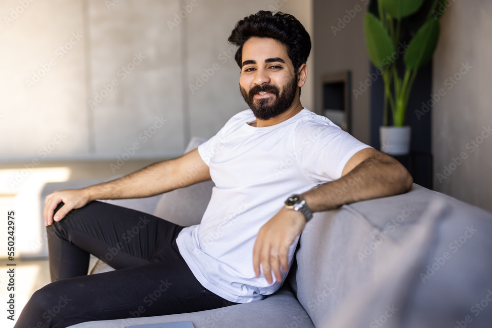 Fototapeta premium Split System. Satisfied Arab man sitting on couch in living room
