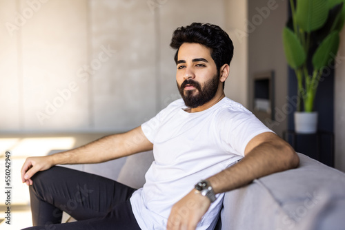 Split System. Satisfied Arab man sitting on couch in living room