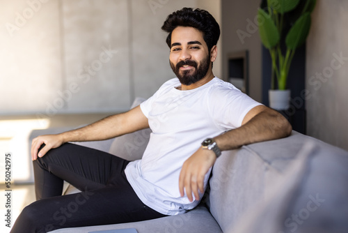 Split System. Satisfied Arab man sitting on couch in living room