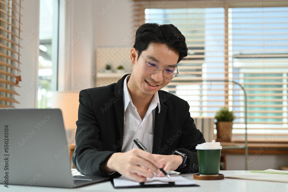 Smiling young businessman working online, searching information on laptop computer Smiling young businessman working online, searching information on laptop computer