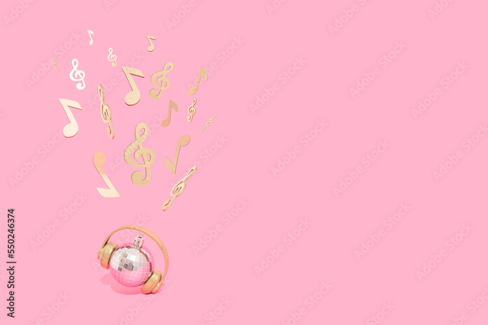 Shiny disco ball with headphones, musical notes and violin keys on a pastel pink  background. Concept of Christmas, New Year and winter holidays party, music and happiness. Good Vibes.