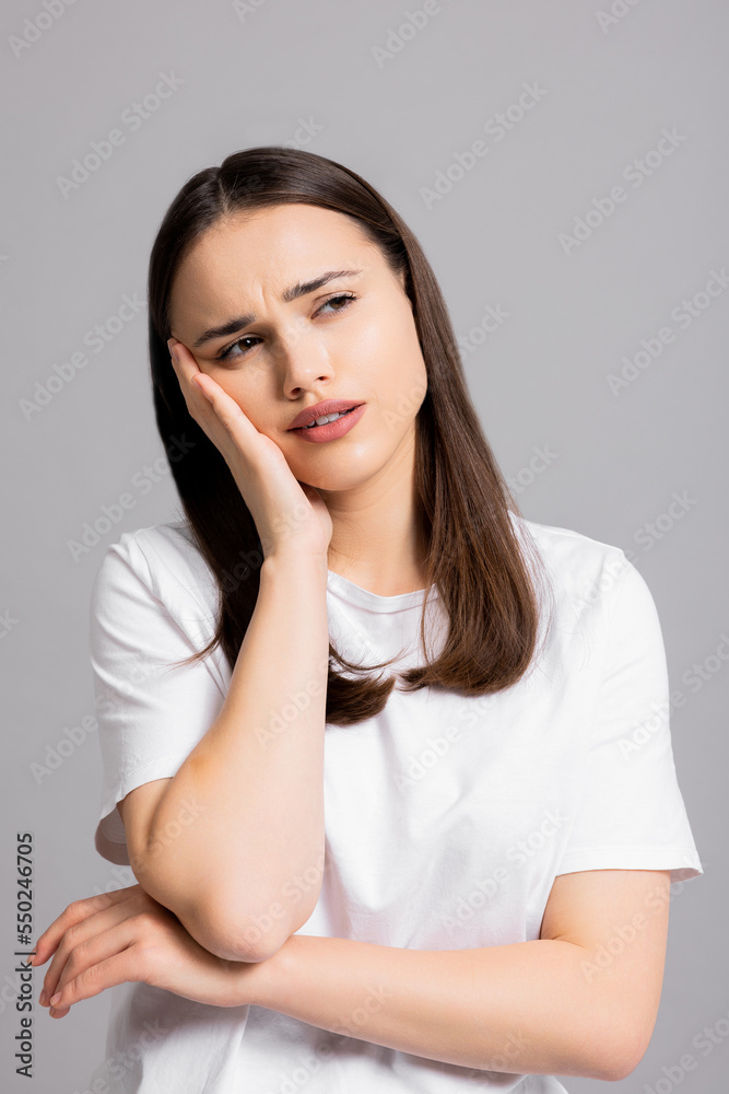 Tired exhausted young girl lady standing on grey background in studio isolated looking into distance holding hand near head showing different sad tired emotions wearing basic white t-shirt. Tired exhausted young girl lady standing on grey background in studio isolated looking into distance holding hand near head showing different sad tired emotions wearing basic white t-shirt.
