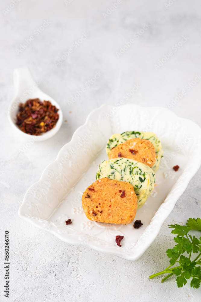 Assorted, salted butter with parsley and butter with paprika and salt, cut into circles, on a white rectangular plate, on a light concrete background. Types of butter for serving dishes.