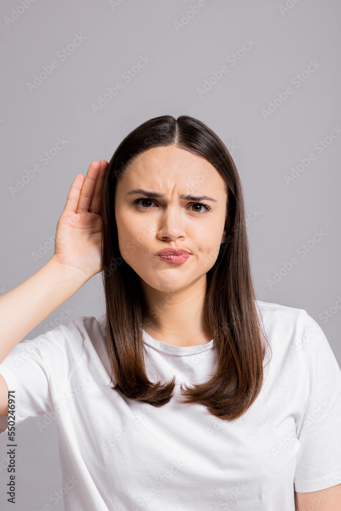 Young curious inquisitive woman girl lady standing on grey background in studio isolated holding hand near ears trying to overhear new information gossip about somebody or discounts. Young curious inquisitive woman girl lady standing on grey background in studio isolated holding hand near ears trying to overhear new information gossip about somebody or discounts.