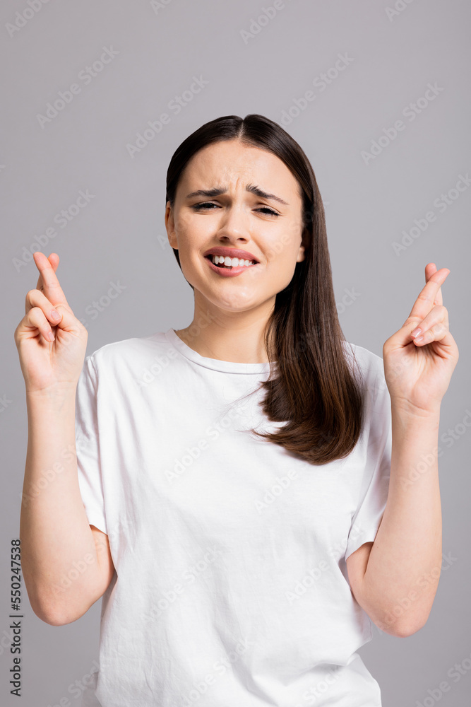 Smiled young girl lady woman wearing white casual t-shirt standing on grey background isolated raising hands crossing fingers looking up smiling dreaming about happy family house and husband. Smiled young girl lady woman wearing white casual t-shirt standing on grey background isolated raising hands crossing fingers looking up smiling dreaming about happy family house and husband.