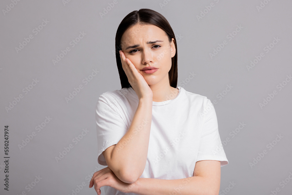 Portrait of cried sad young woman wearing white casual t-shirt standing on grey background in studio isolated. Girl suffering from abuse domestic volatile desperate woman. Portrait of cried sad young woman wearing white casual t-shirt standing on grey background in studio isolated. Girl suffering from abuse domestic volatile desperate woman.