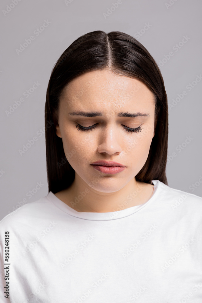 Close up shot selective focus autumn depressive mood expressions sad cried young woman standing on grey background in studio isolated wearing white t-shirt looking down desperation.
