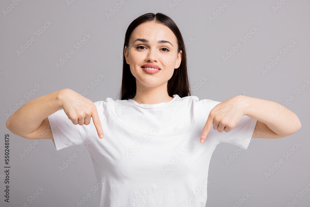 Portrait of young beautiful woman pointing fingers down smiling, showing banner, click on link below gesture, inviting people to follow, standing over white background. Portrait of young beautiful woman pointing fingers down smiling, showing banner, click on link below gesture, inviting people to follow, standing over white background.