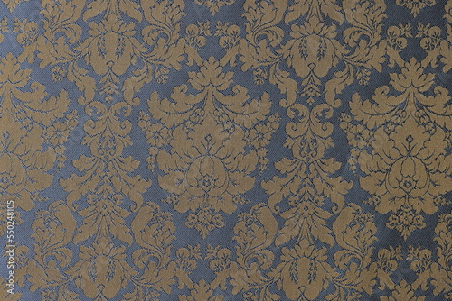 Golden-blue fabric with ornament of flowers and leaves as background.