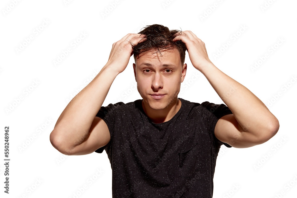 Fototapeta premium Young handsome man in casual T-shirt combs his hair with hands. Well-being. Concept of men's health, body and hair care
