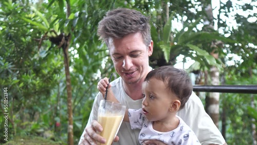 Young father with little son enjoying a glass of fruitshake outdoor in nature. photo