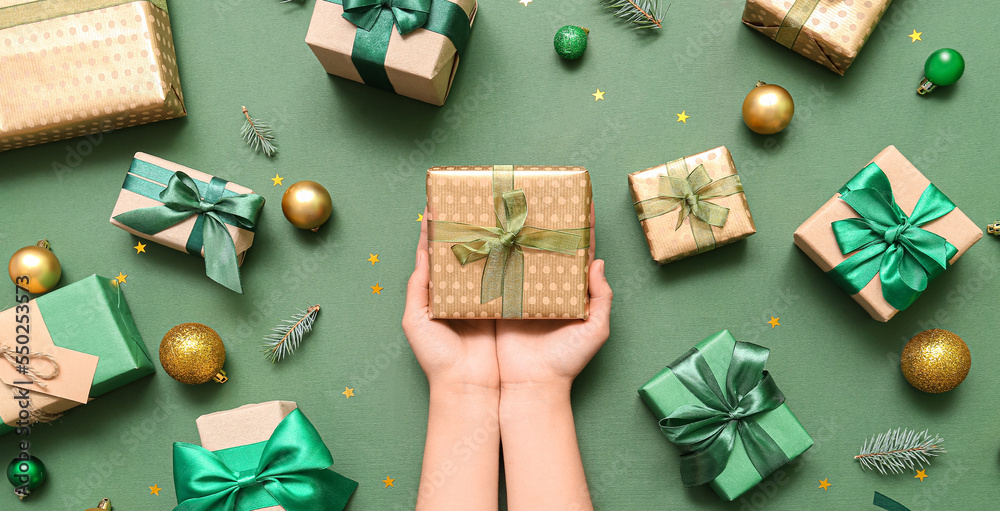 Female hands with gift boxes and Christmas balls on green background
