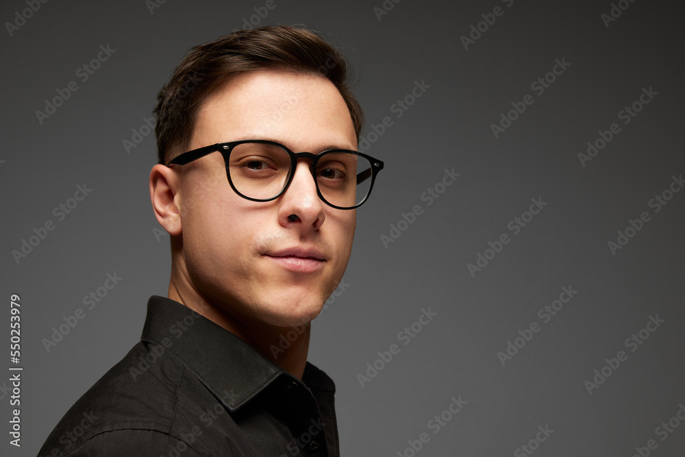 Closeup. Young businessman in black business classic style shirt looks at camera with confident look isolated over grey background. Fashion look of businessman. Closeup. Young businessman in black business classic style shirt looks at camera with confident look isolated over grey background. Fashion look of businessman.