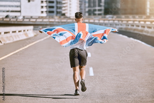 Winner, flag and fitness man running on the city road celebrates winning achievement in summer. Sports, training and competitive British male runner doing healthy exercise in celebration outside