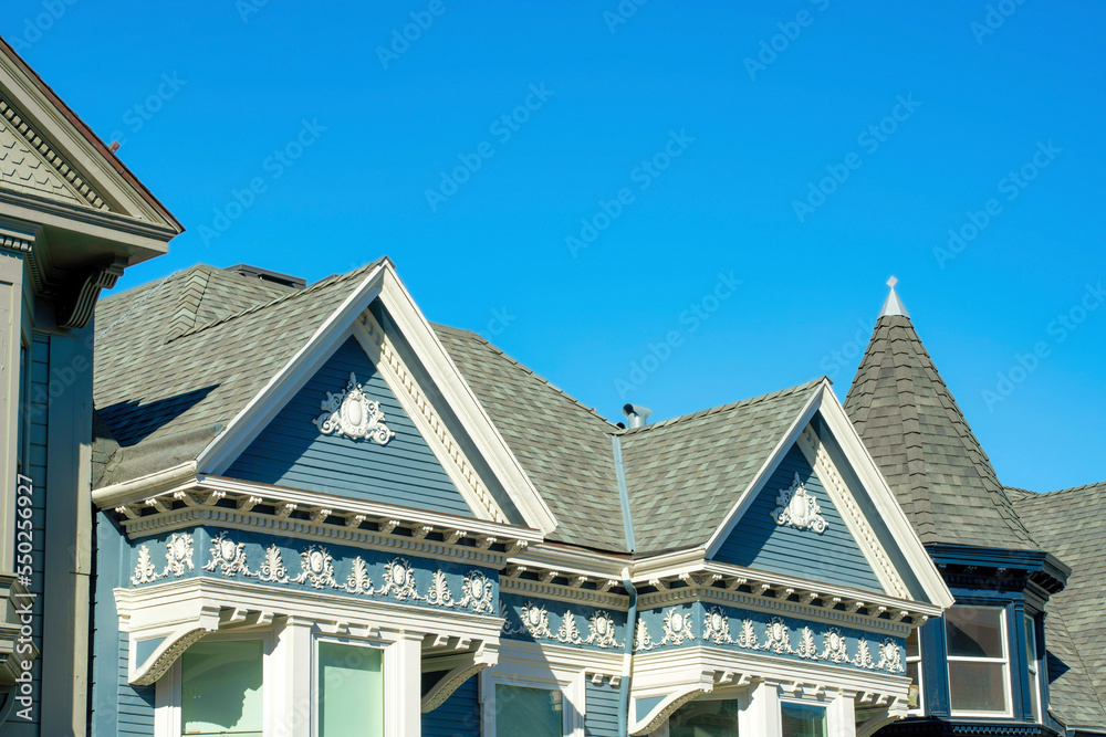 Double gable style roofs on house or home with blue wooden exterior and white accent paint on victorian home with light roof tiles
