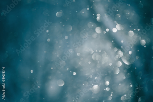 Blurred snowflakes in morning light in winter forest. Glowing bokeh abstract background.