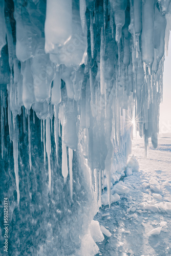 Ice cave with icicles on Baikal lake at sunset. Blue ice in the evening sunlight. © smallredgirl