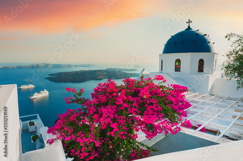 Santorini island, Greece. White architecture with pink flowers at sunset.
