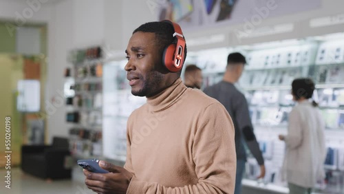 An African man in an eleutronics store chooses wireless headphones for himself. The man tests the sound, and shakes his head. photo