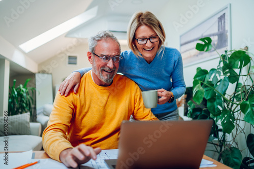 Senior middle aged happy couple using laptop together at home