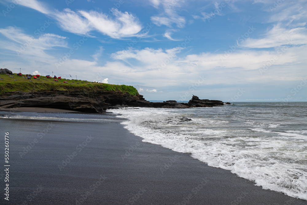 A rocky shore with a beautiful beach (Love beach) with black sand at Kedunggu Beach, near Tanah Lot temple. Bali, Indonesia