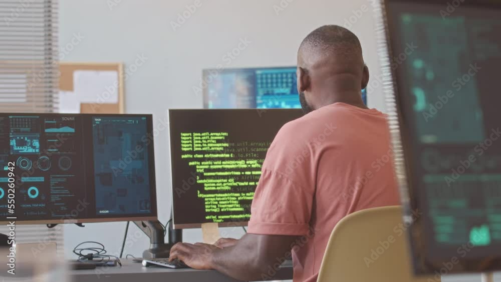 Focused African American male programmer typing lines of html code on computer while working in contemporary equipped office Focused African American male programmer typing lines of html code on computer while working in contemporary equipped office