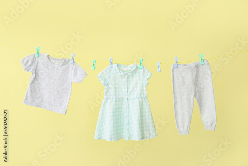 Different baby clothes hanging on rope against yellow background
